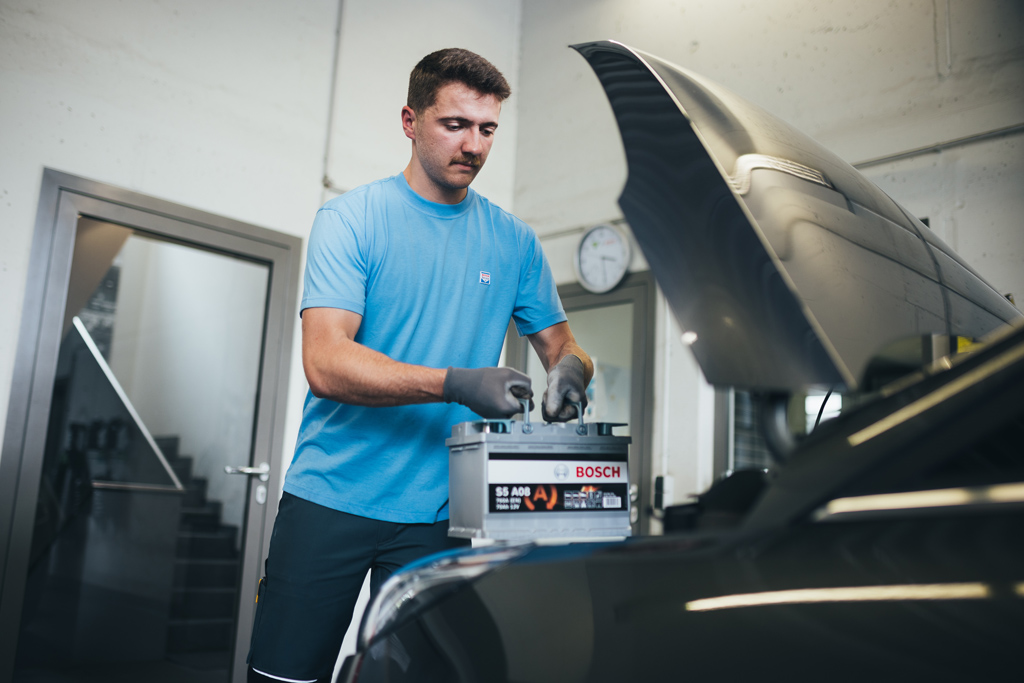 Technician fitting a Bosch car battery under a vehicle bonnet