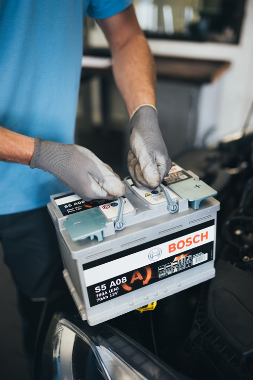 Mechanic fitting a Bosch S5 A08 AGM car battery during a vehicle battery replacement