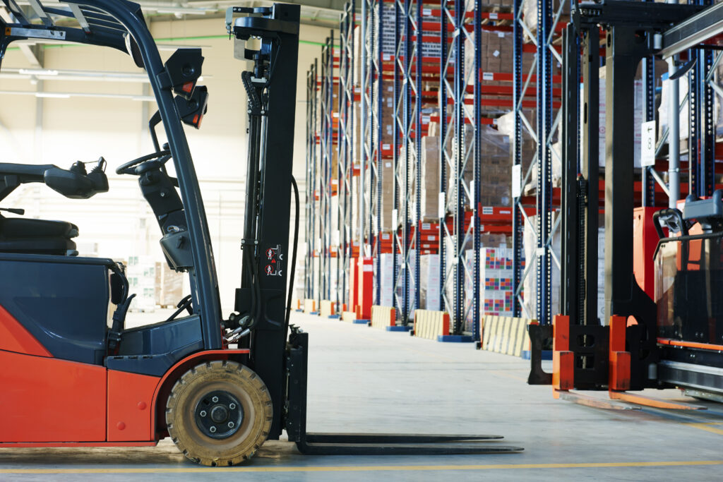 Forklift truck in a large warehouse with tall storage racking and palletised goods