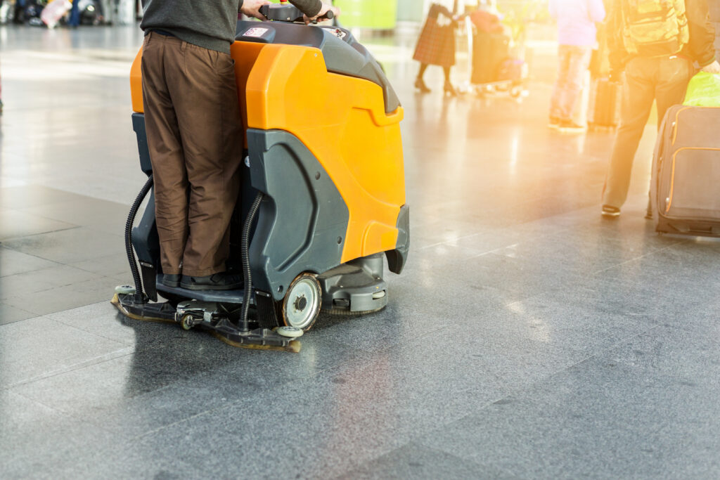 Operator using a ride-on floor scrubber machine in a busy public building
