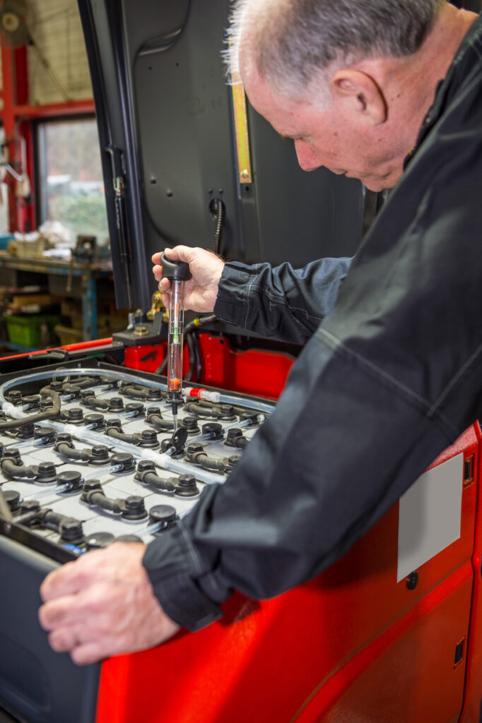 Technician checking industrial forklift battery electrolyte levels with a hydrometer